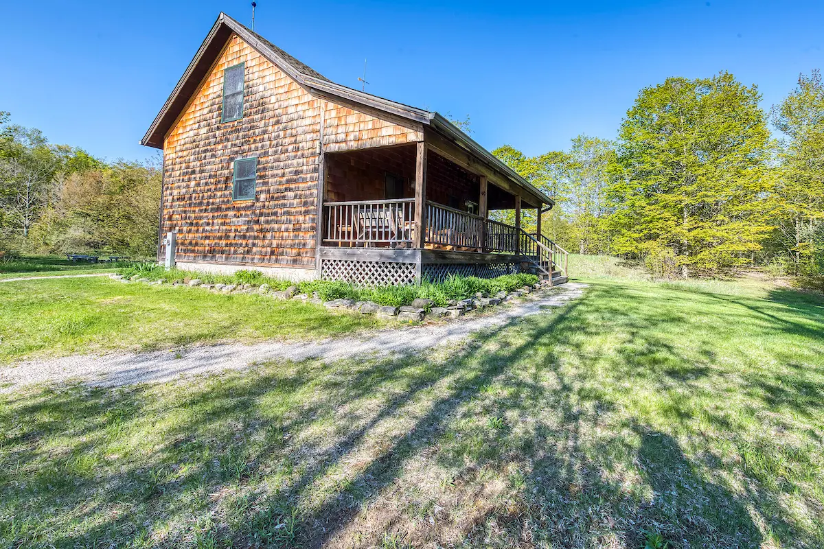 A wooden house with a porch and trees in the background.