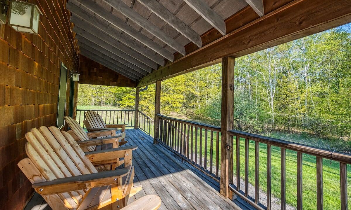 A porch with wooden chairs and benches on it.